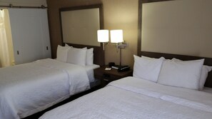 A hotel room with two single beds, a nightstand with a lamp, and a large mirror above the beds.