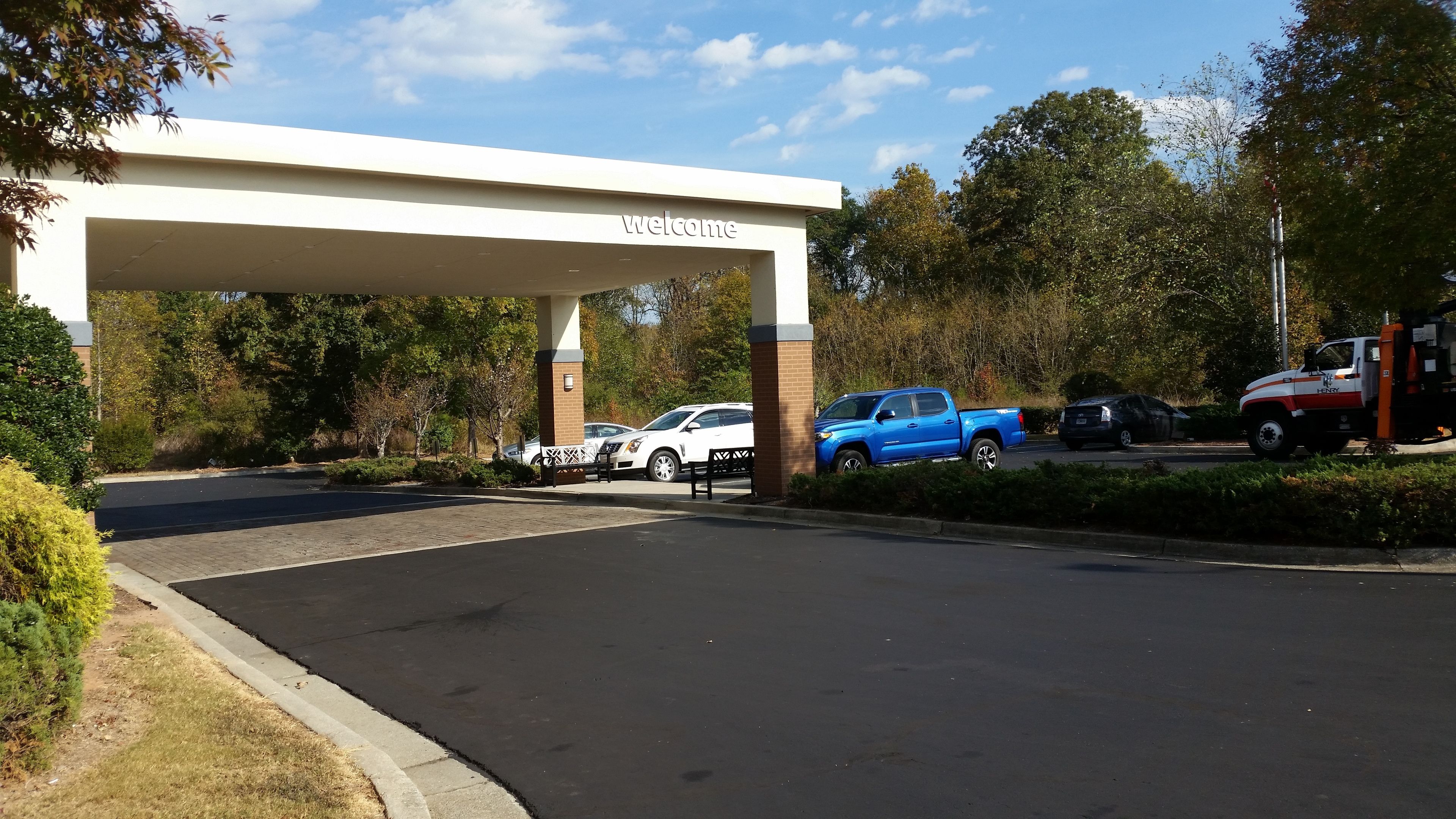 A gas station with a 'Welcome' sign, a parking area with several cars, and a truck.