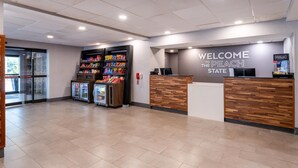 A hotel reception area with a 'Welcome to the Peach State' sign, a reception desk, a refrigerator stocked with snacks, and a glass door entrance. - Hampton Inn Commerce (Commerce)