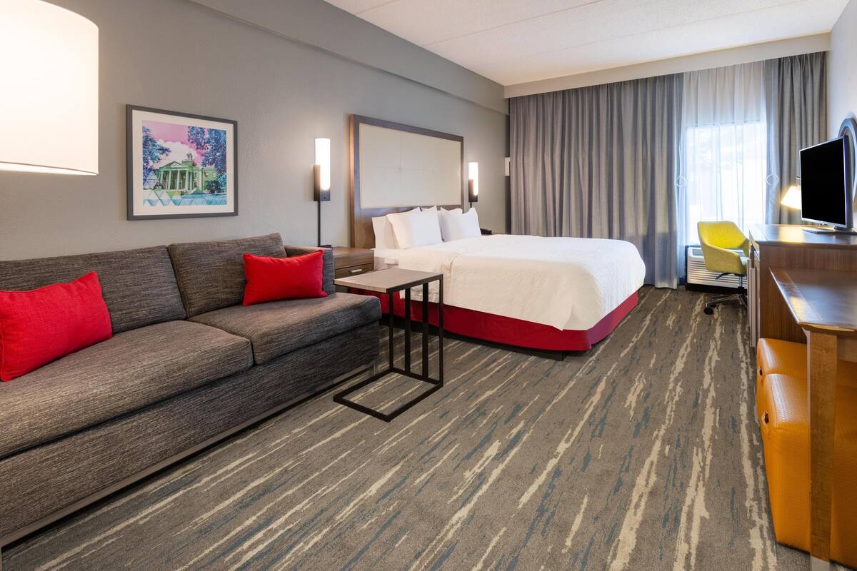 Una habitación de hotel con cama, sofá, escritorio, silla y televisor.