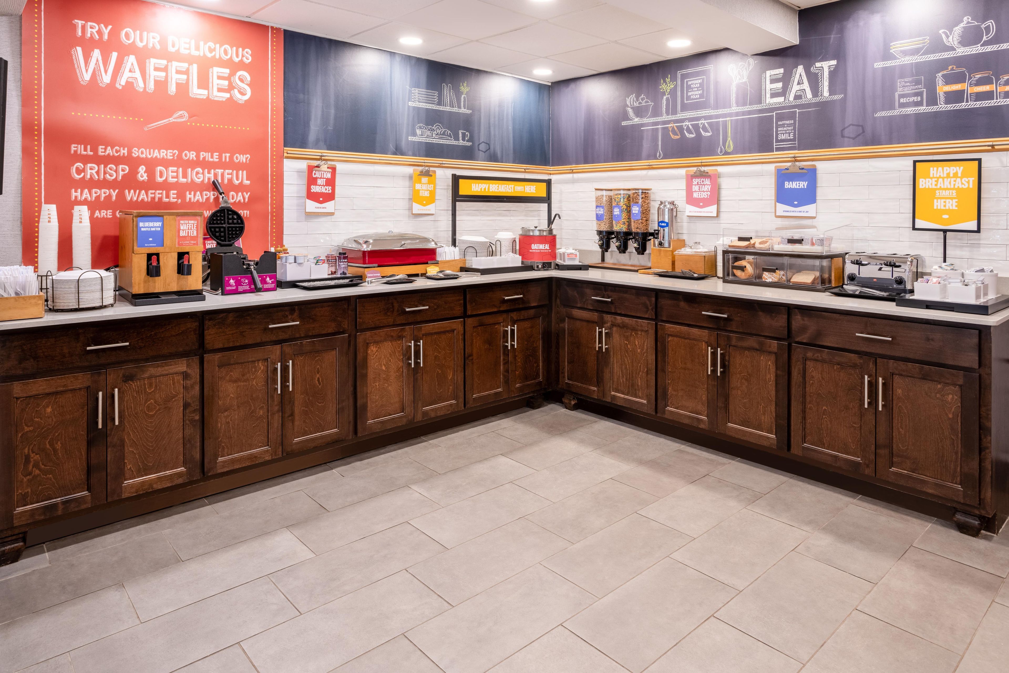 Un espace cuisine équipé de postes pour préparer des gaufres, avec des produits pour le petit-déjeuner, et une affiche faisant la promotion des gaufres.