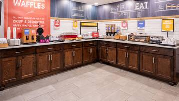 Un espace cuisine équipé de postes pour préparer des gaufres, avec des produits pour le petit-déjeuner, et une affiche faisant la promotion des gaufres.