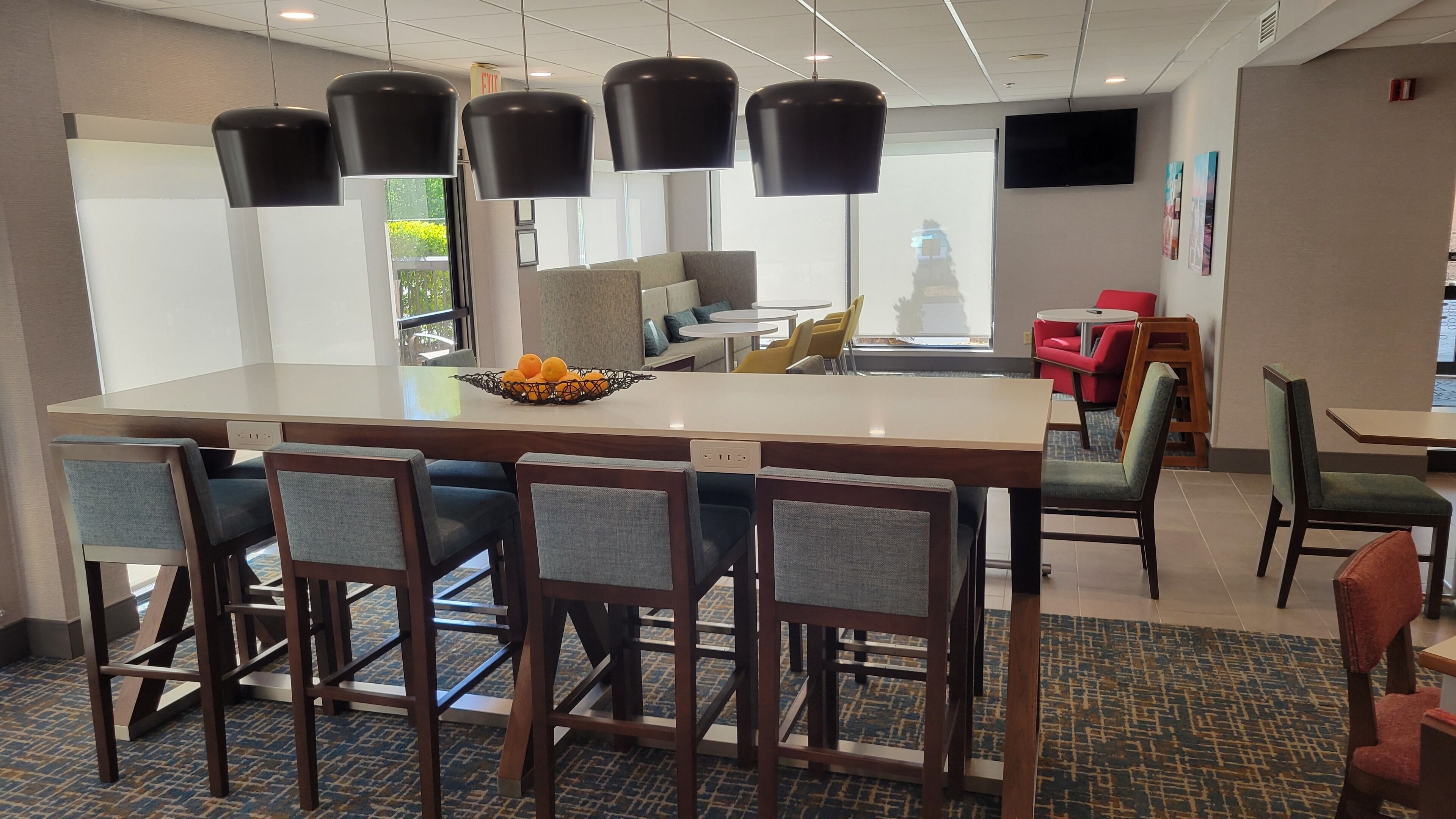 A modern hotel lobby with a central island, bar seating, and a television mounted on the wall.