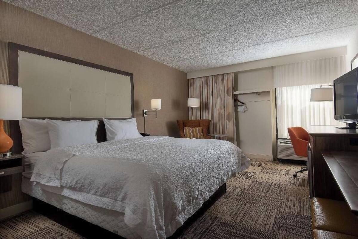 Habitación de hotel con una cama grande, dos mesitas de noche, un escritorio con silla, un televisor y una ventana con cortinas.