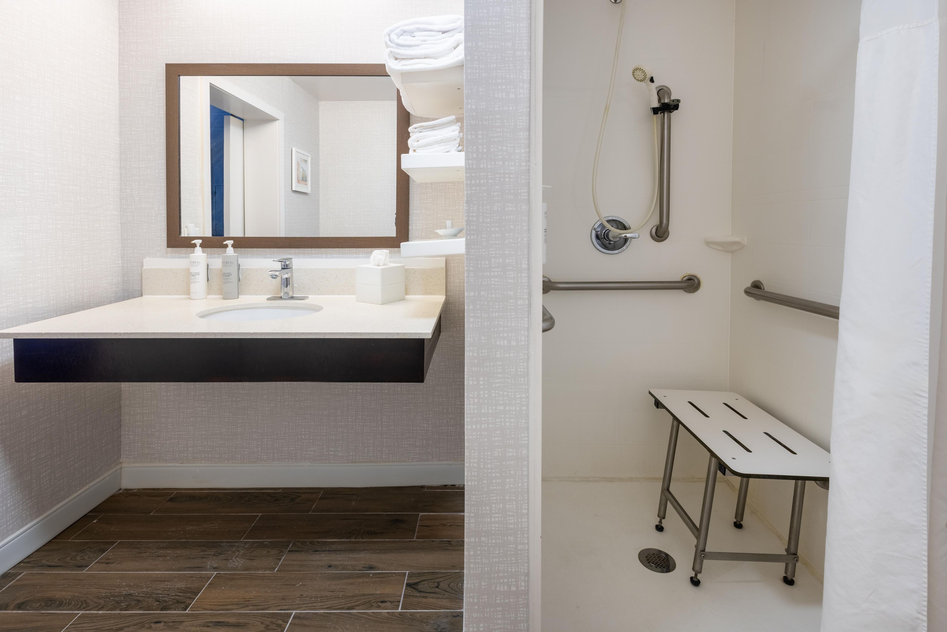 A bathroom with a modern sink, mirror, and shower area with grab bars.