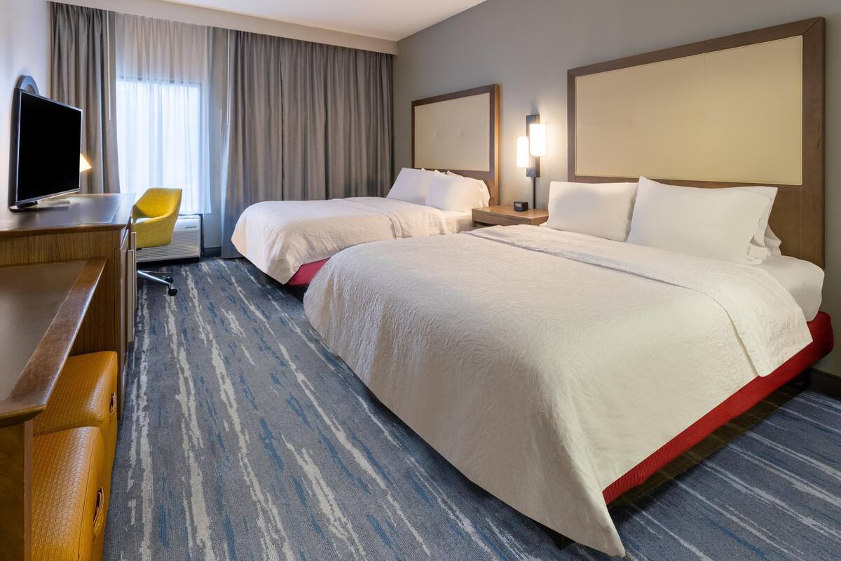 Una habitación de hotel con dos camas, un escritorio con televisor y una silla.