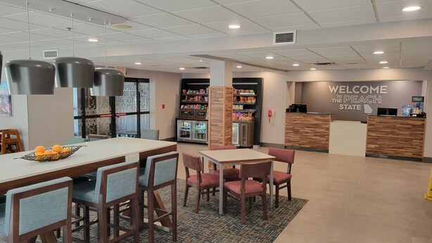 A hotel lobby with a reception desk, a seating area with tables and chairs, and a refrigerator stocked with beverages. - Hampton Inn Commerce (Commerce)