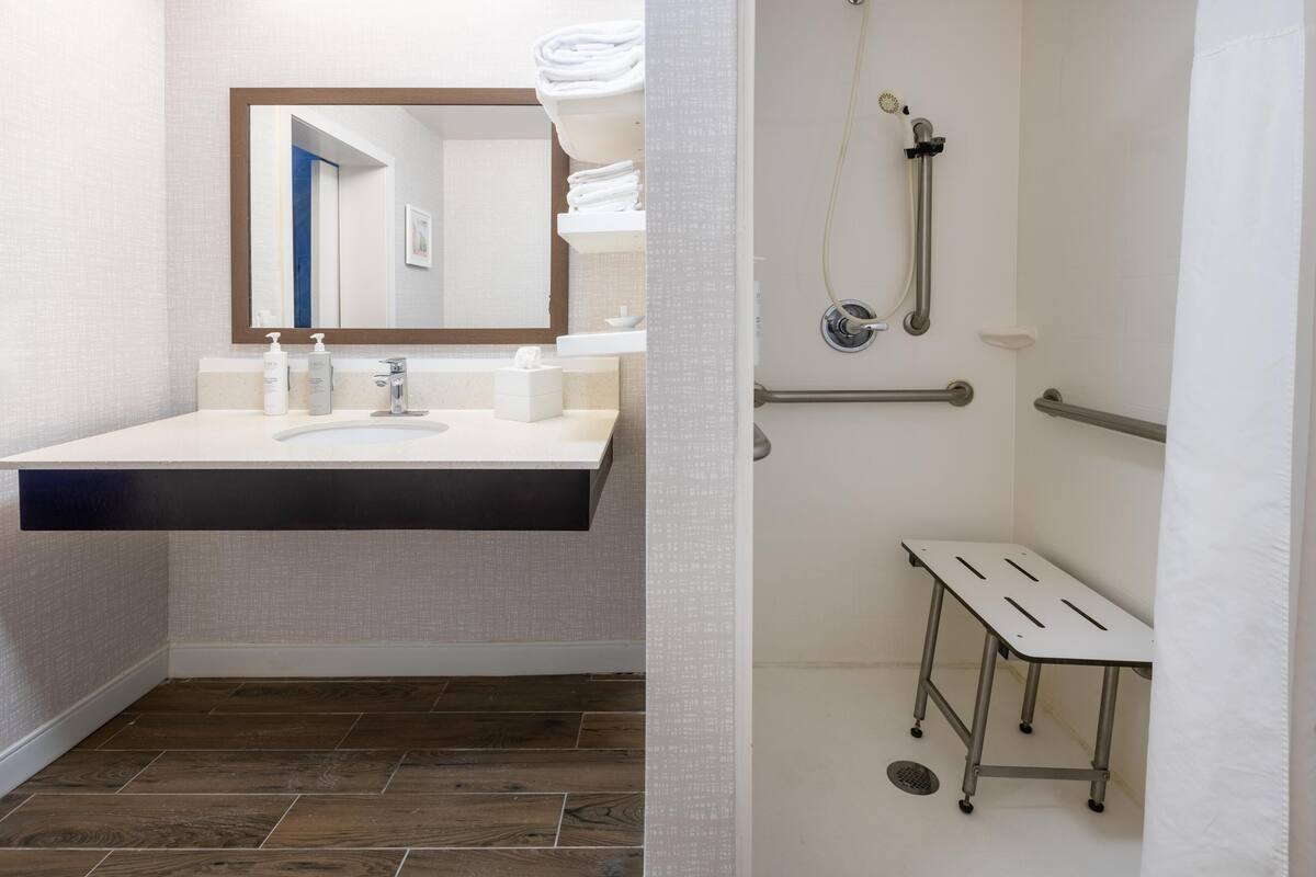 Un baño moderno con un espejo grande, un lavabo y una ducha con barras de apoyo.