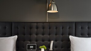 Une chambre d’hôtel moderne avec une tête de lit capitonnée, deux lits, une table de chevet avec une horloge et une plante, et deux lampes suspendues.