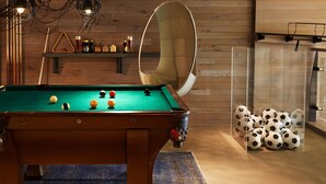 Une table de billard avec des billes, un fauteuil suspendu et une vitrine contenant des ballons de football.