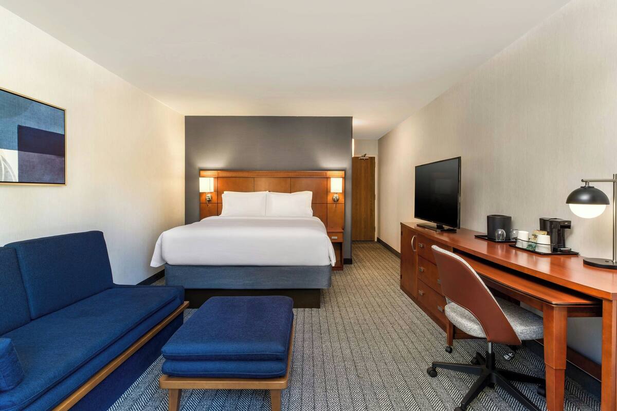 Una habitación de hotel con cama, escritorio con televisor, sofá y cafetera.