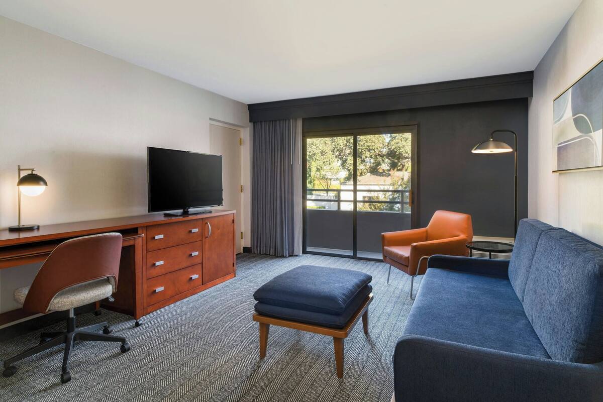 Habitación de hotel con escritorio, televisión, sofá y vistas al exterior.