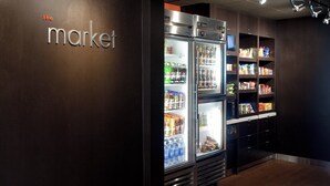 Un expositor refrigerado con diversas bebidas y aperitivos, un letrero que dice "the market", y estantes llenos de productos envasados.