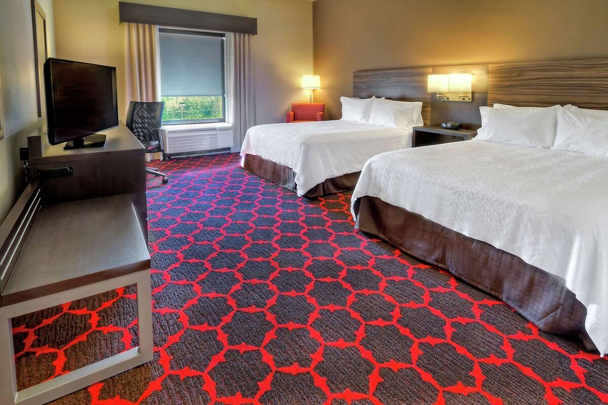A hotel room with two beds, a TV, a desk, and a window with curtains.