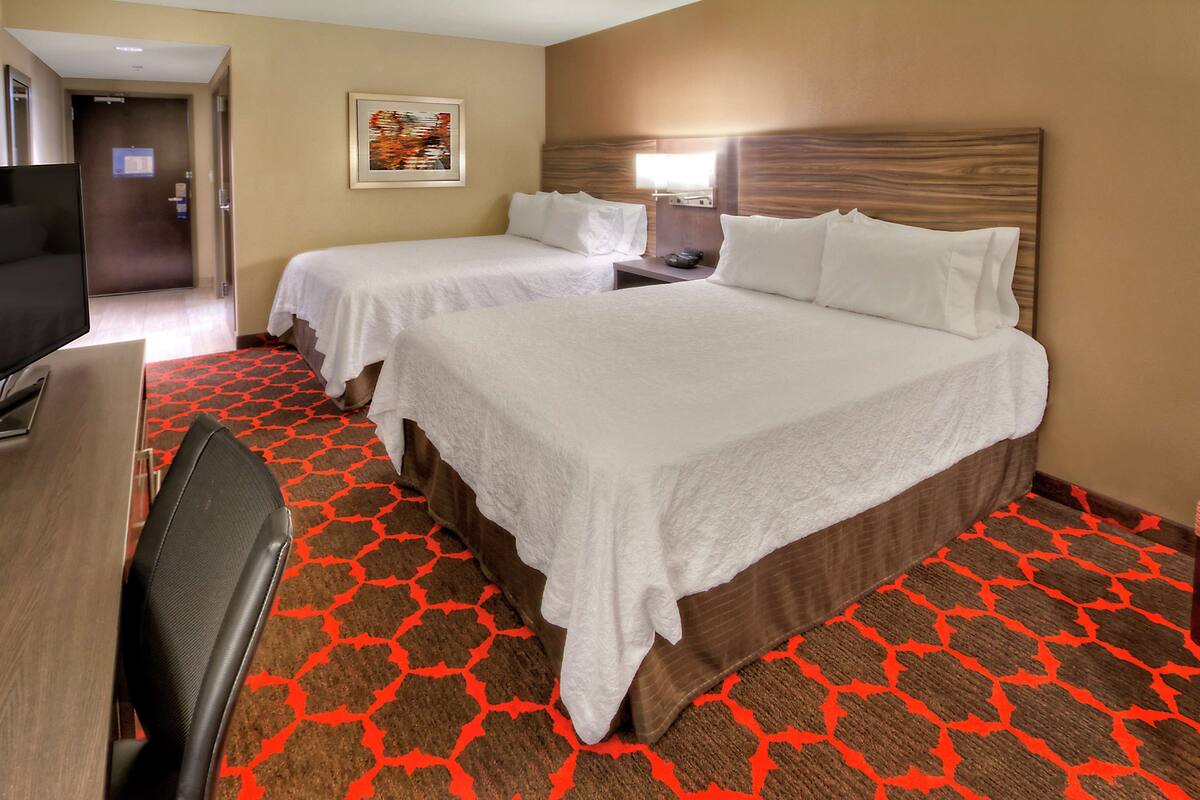 A hotel room with two beds, a desk, a TV, and a patterned carpet.
