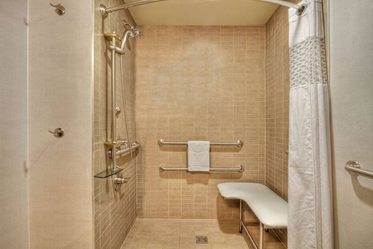 A shower area with a glass door, a towel rack, and a bench.