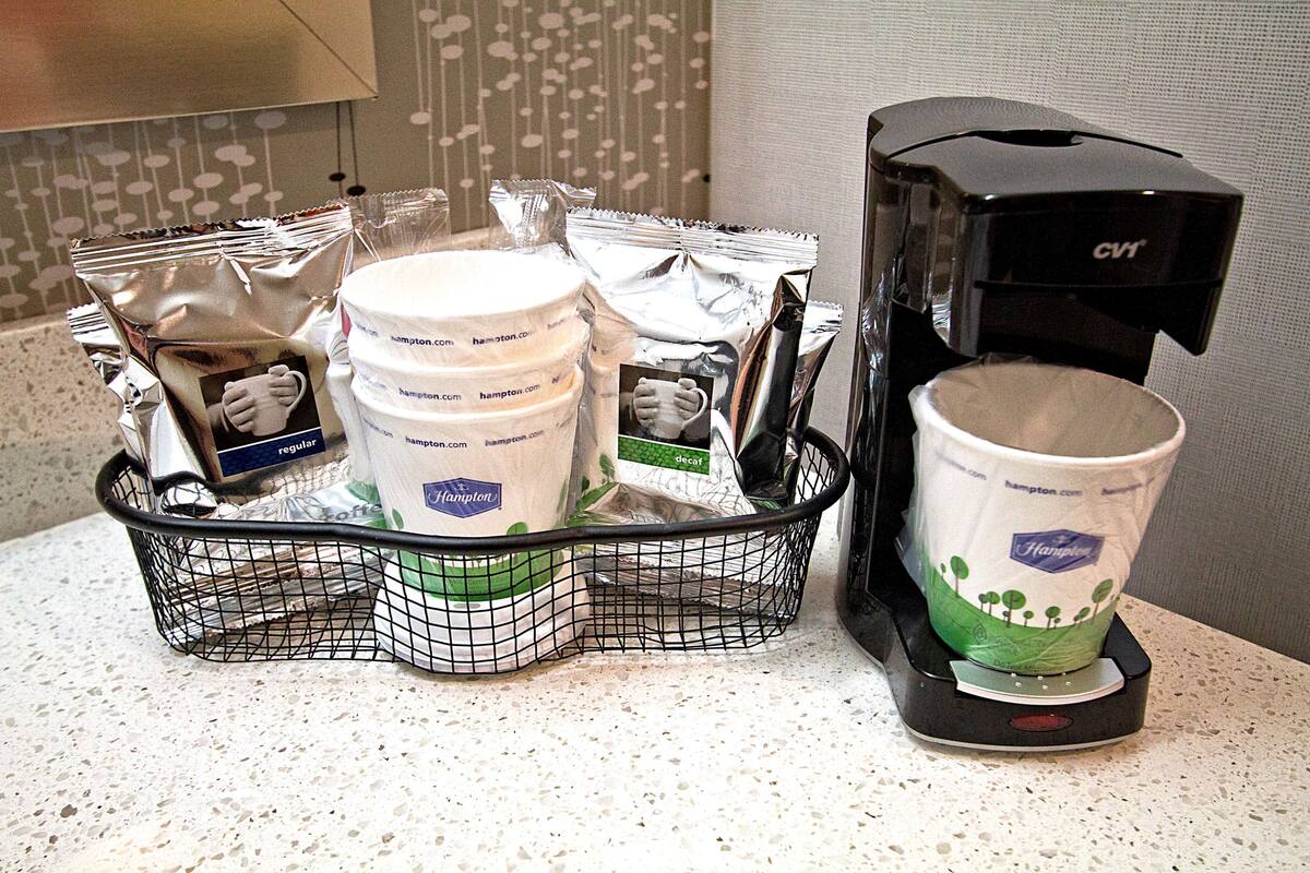 A coffee machine and a basket with disposable cups and coffee pods on a countertop.
