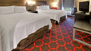 Ein Hotelzimmer mit zwei Betten, einem Fernseher, einem Schreibtisch und einem Fenster mit Vorhängen.