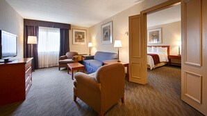 Una habitación de hotel con televisión, sofá, sillón, escritorio y cama.