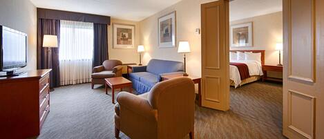 Une chambre d’hôtel équipée d’une télévision, d’un canapé, d’un fauteuil, d’un bureau et d’un lit.
