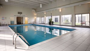 Una piscina interior con marcas claras de profundidad, un letrero que indica agua poco profunda y un letrero que prohíbe el clavado.