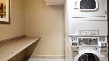 A laundry room with a stacked washer and dryer, a countertop, and a framed picture on the wall.