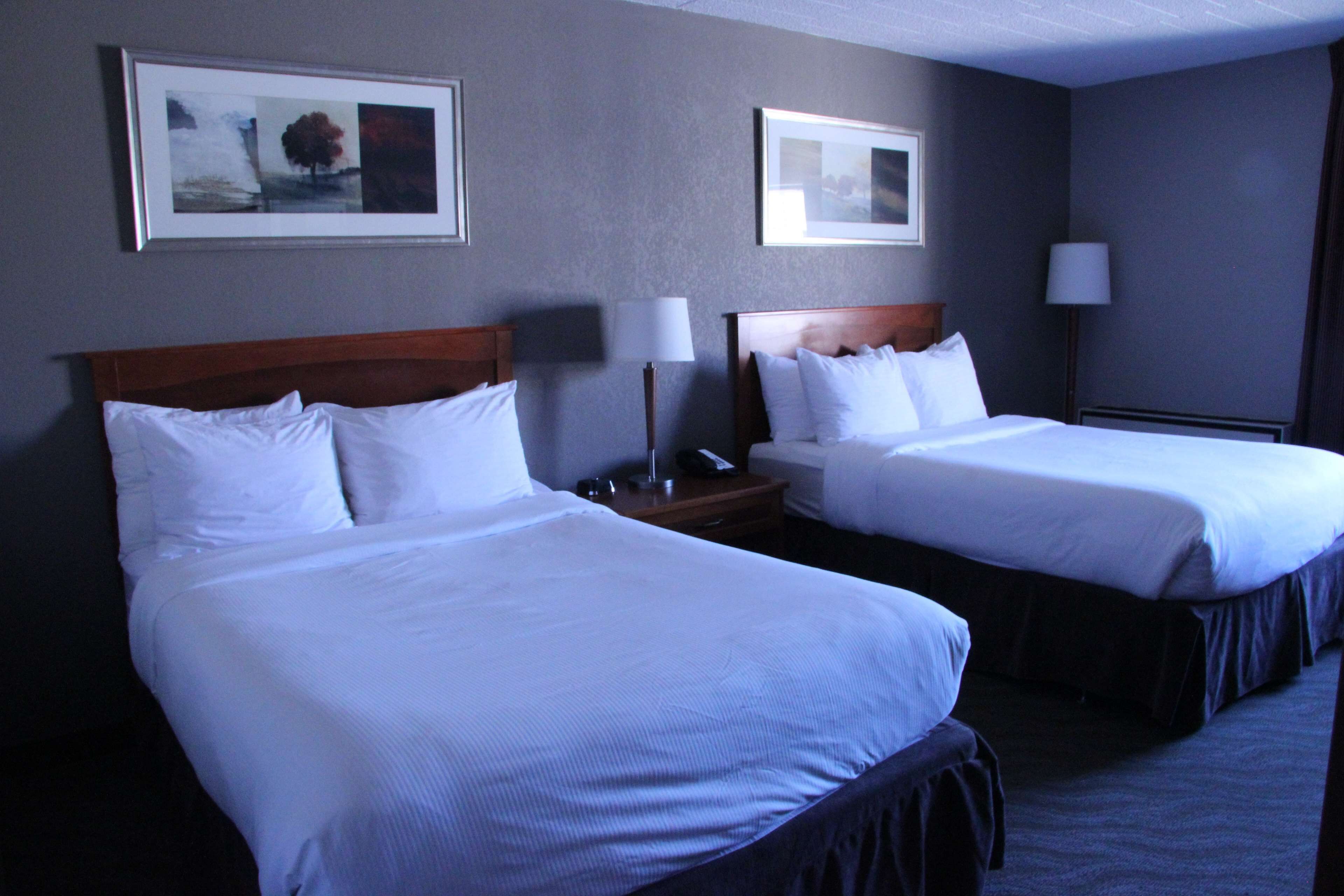 A hotel room with two beds, a nightstand with a lamp, and framed artwork on the walls.