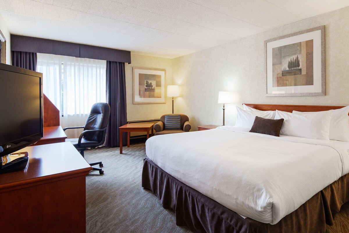 A hotel room with a large bed, a desk with a television, a chair, and two bedside tables with lamps.