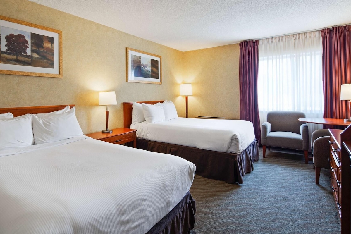 A hotel room with two beds, a desk, a chair, and two framed pictures on the wall.