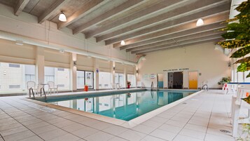 Una piscina interior con suelo de baldosas, un cartel que indica agua poco profunda y una advertencia sobre no bucear.