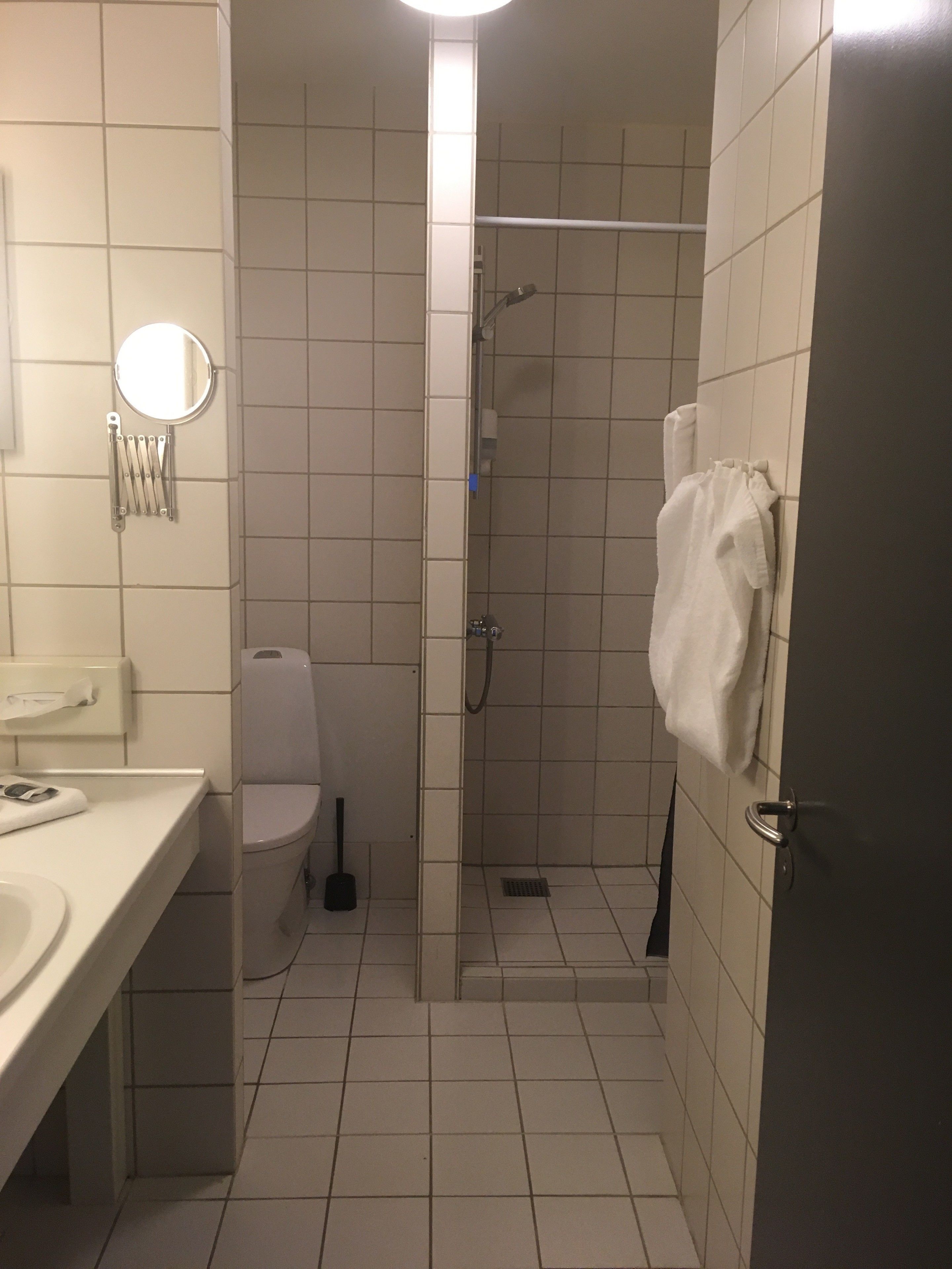Ein kleines Badezimmer mit Fliesen, einer Toilette, einem Waschbecken, einem Spiegel und einer Duschkabine.