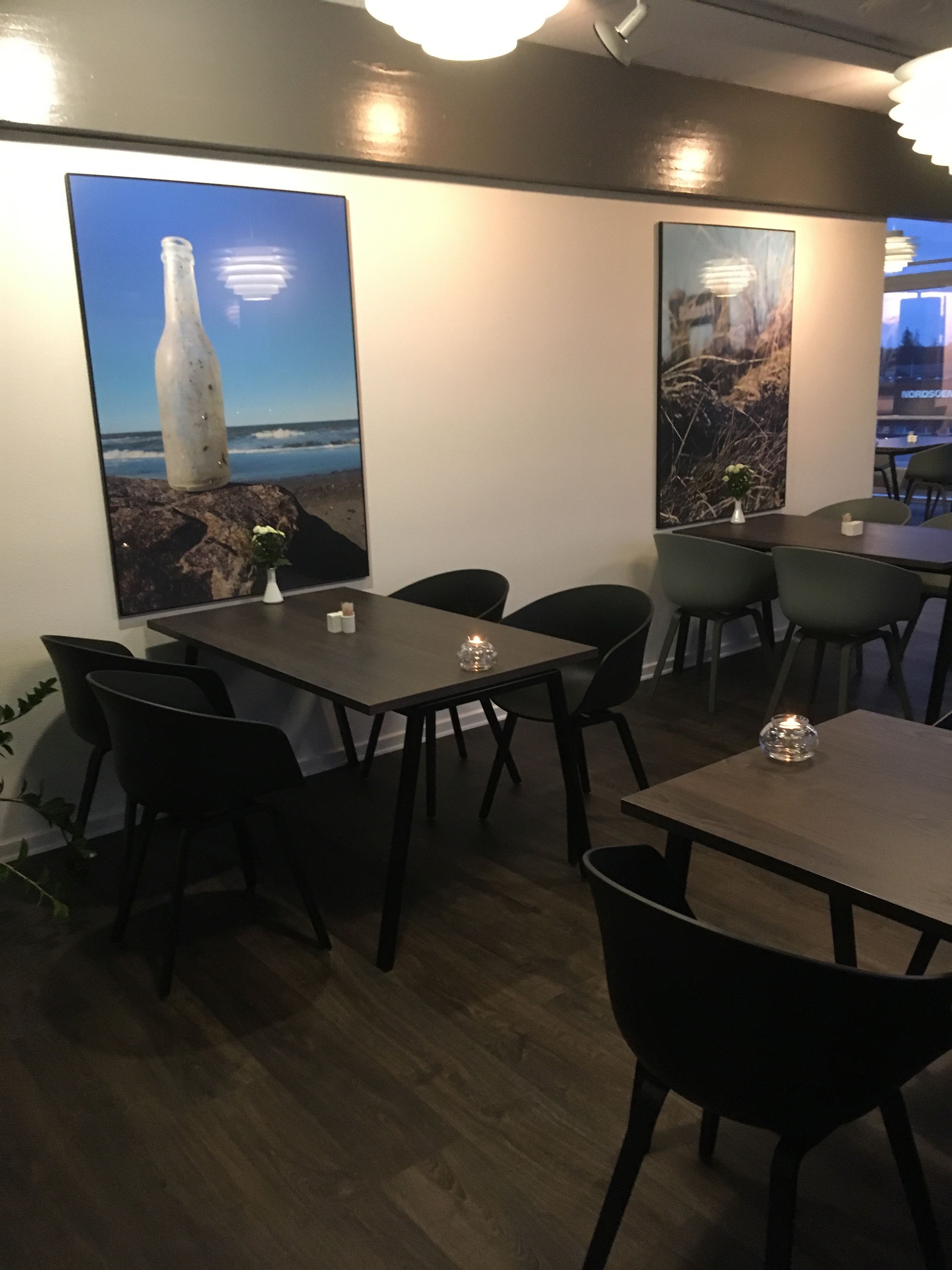 Un comedor con mesas y sillas, un florero con flores y dos grandes obras de arte mural que muestran una botella y un paisaje.