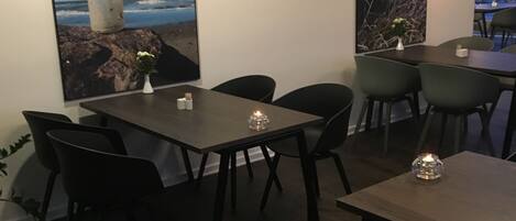 Un comedor con mesas y sillas, un florero con flores y dos grandes obras de arte mural que muestran una botella y un paisaje.