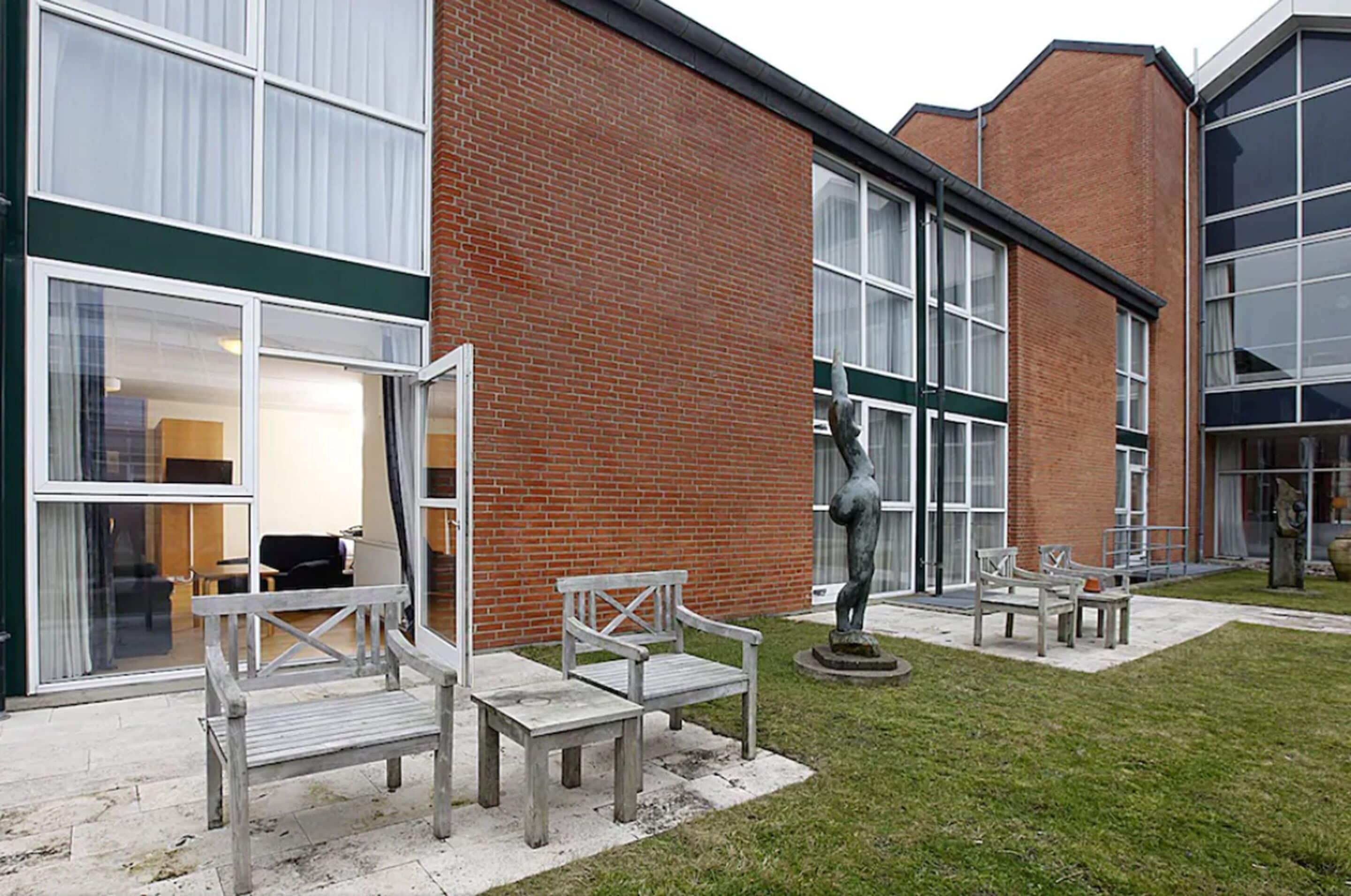A building with a brick facade, large windows, and outdoor seating with benches and a statue.