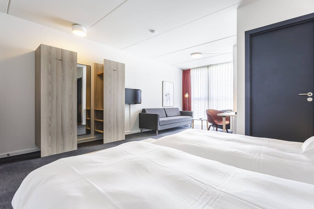 A hotel room with a large bed, a desk with a chair, a television, and a wardrobe.