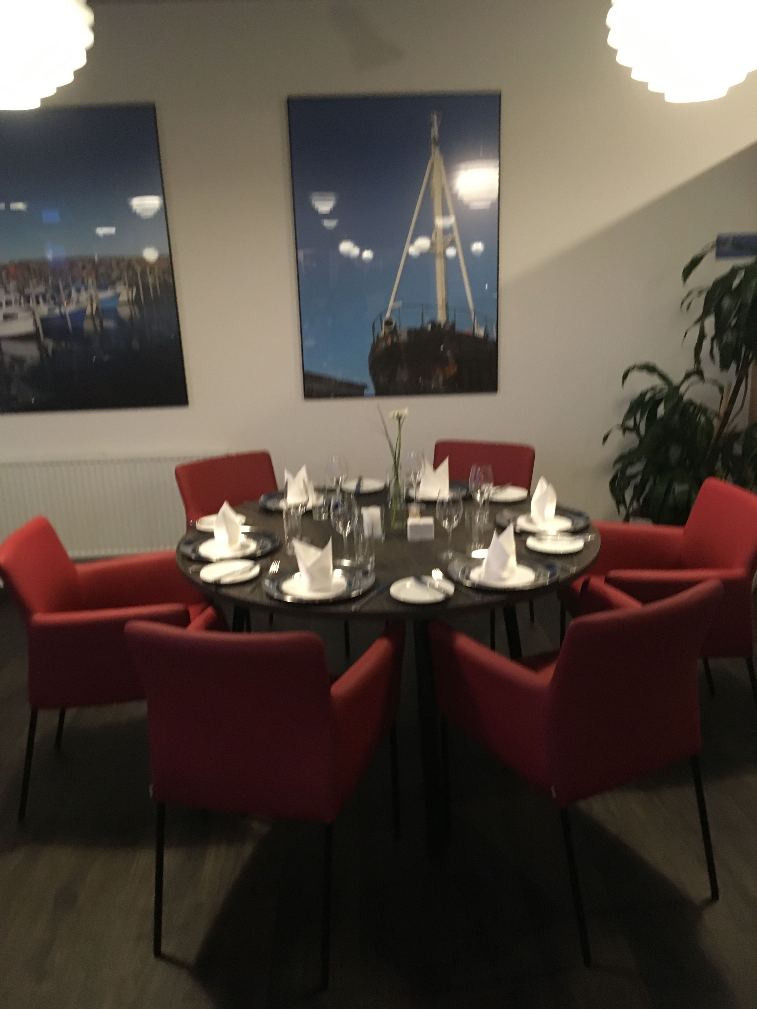 A dining area with a round table set for six, surrounded by red chairs. There are two framed pictures on the wall above the table.