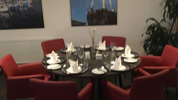 Ein Essbereich mit einem runden Tisch, gedeckt für sechs Personen, umgeben von roten Stühlen. Über dem Tisch hängen zwei gerahmte Bilder an der Wand.