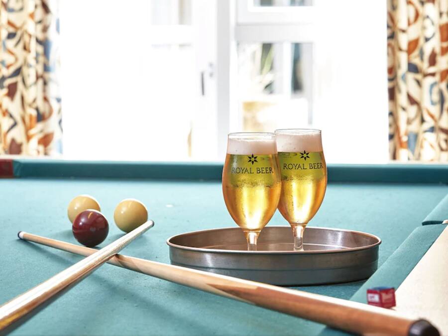 Een pooltafel met twee glazen Royal Beer, poolkeus en biljartballen.