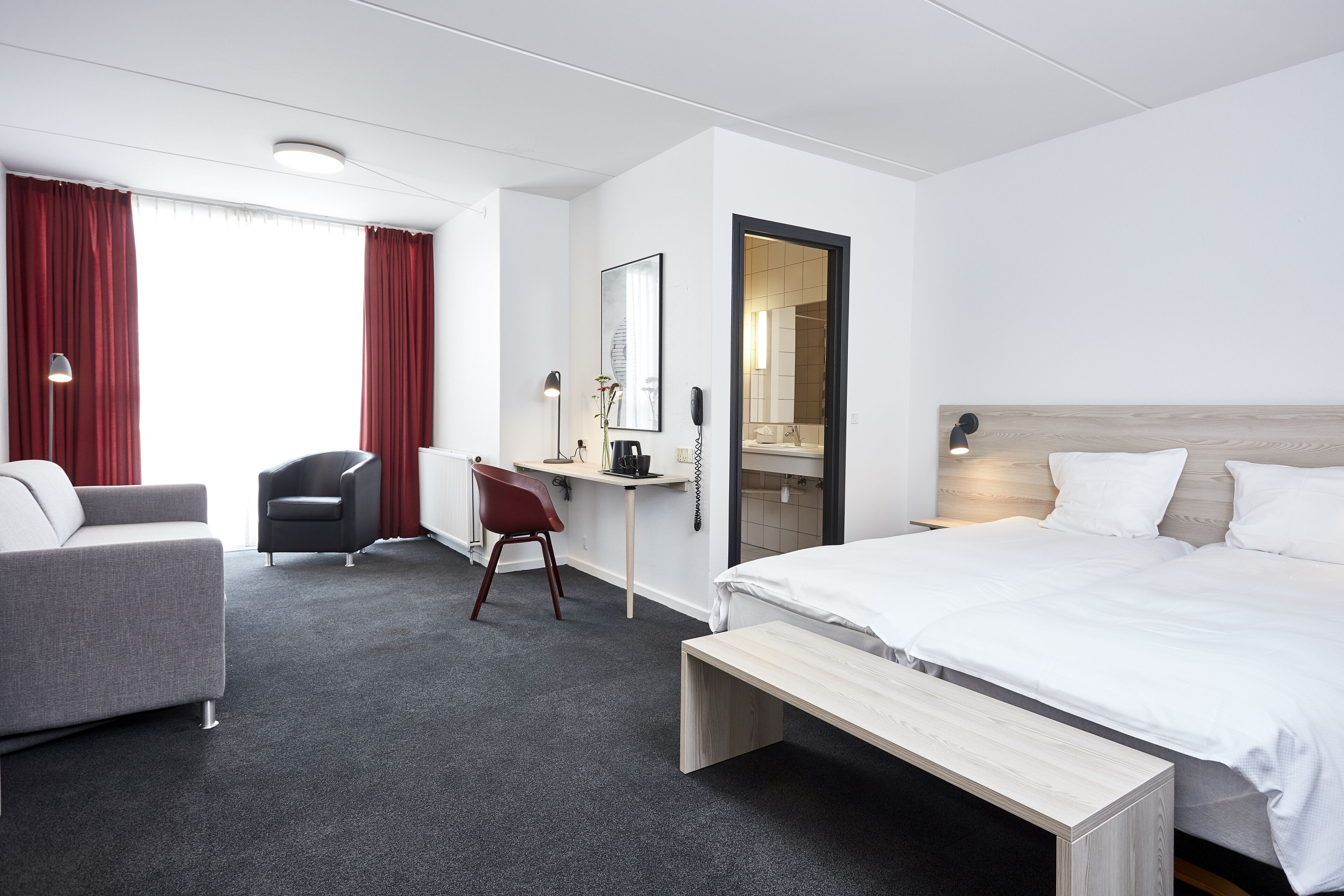 A hotel room with a bed, a desk, a chair, a sofa, and a bench.