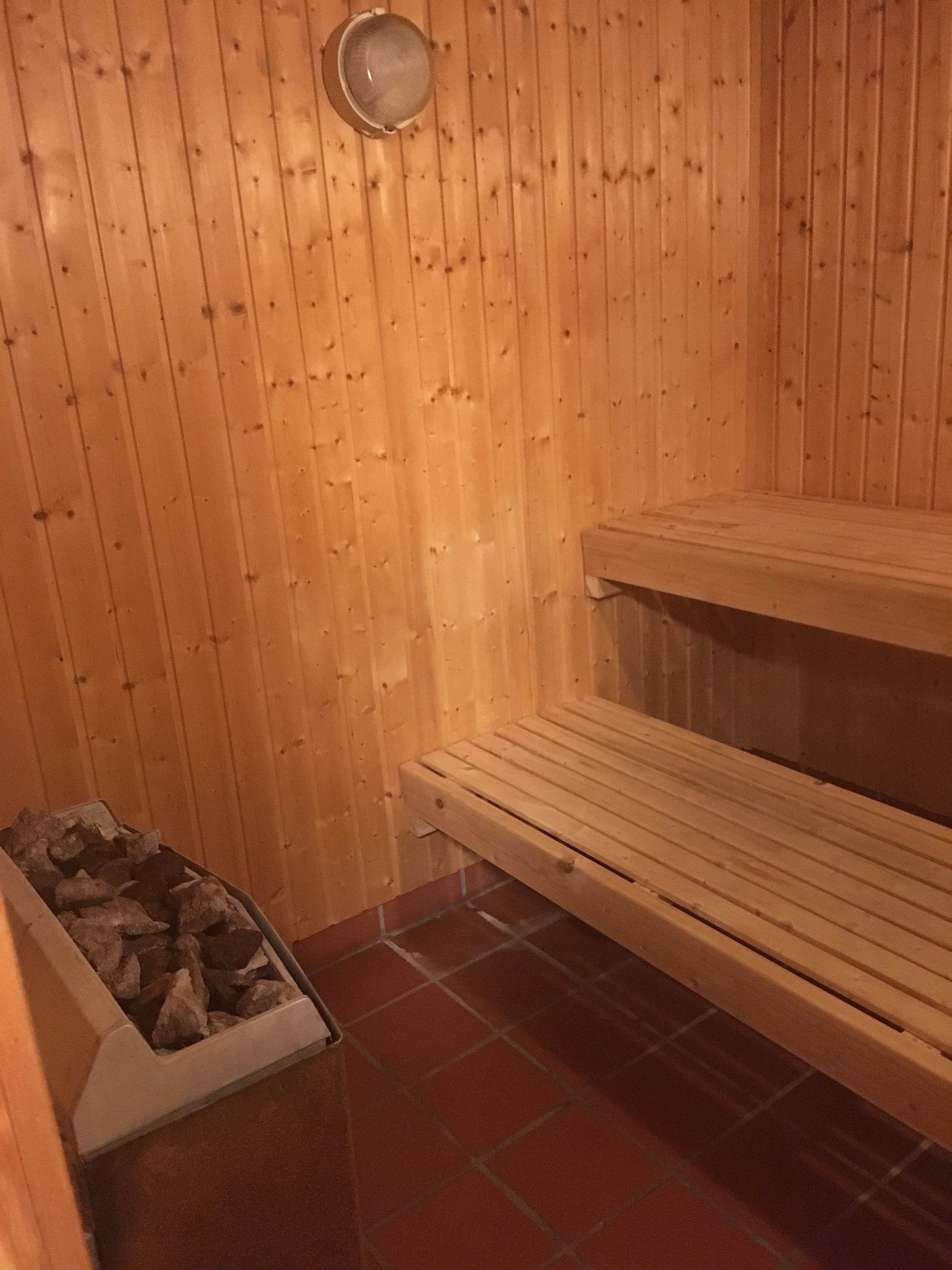 A wooden sauna with benches and a stone-filled container.