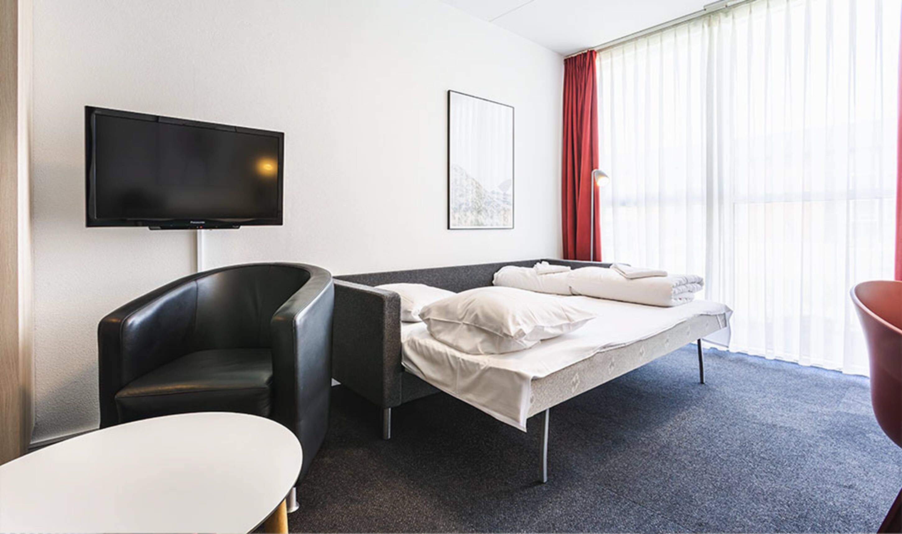 Ein Hotelzimmer mit einem Bett, einem Sessel, einem Fernseher und einem fenster mit Vorhängen.