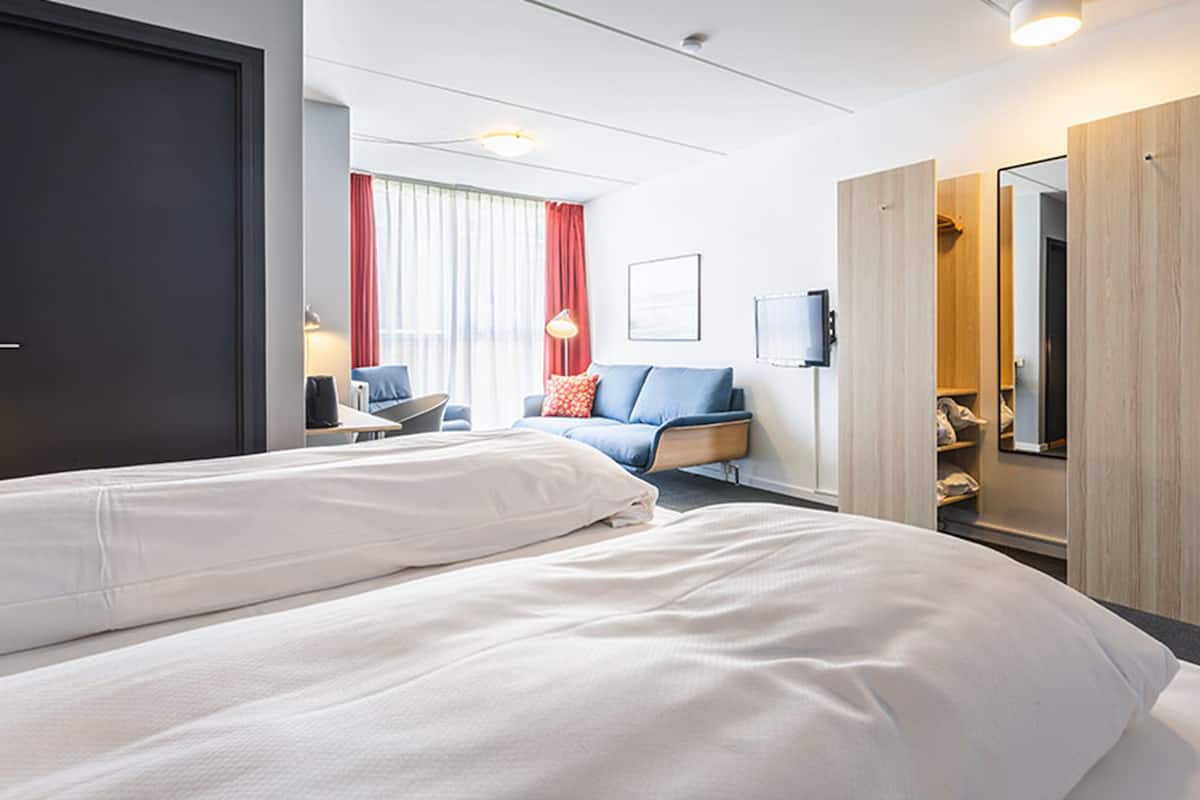 A hotel room with two beds, a desk, a chair, a TV, and a wardrobe.