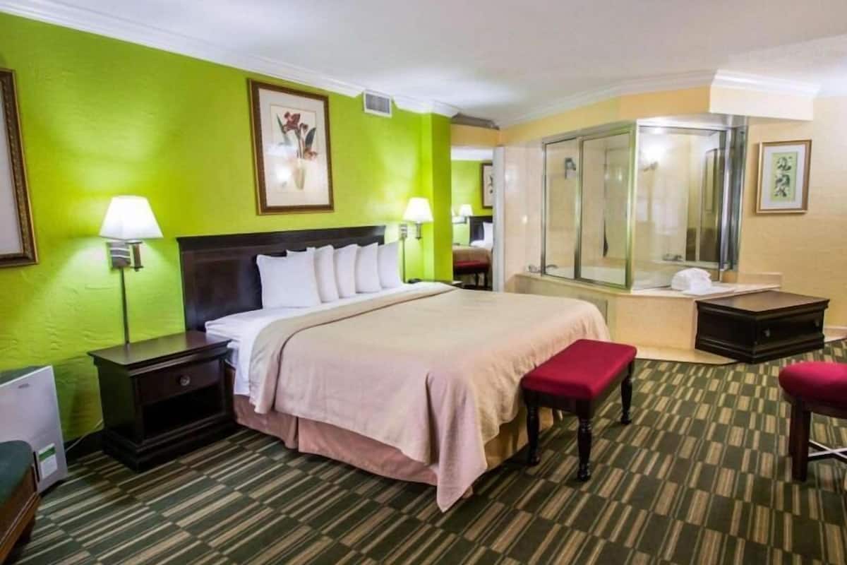 A hotel room with a bed, bedside tables, a bench, a shower, and a mirror.