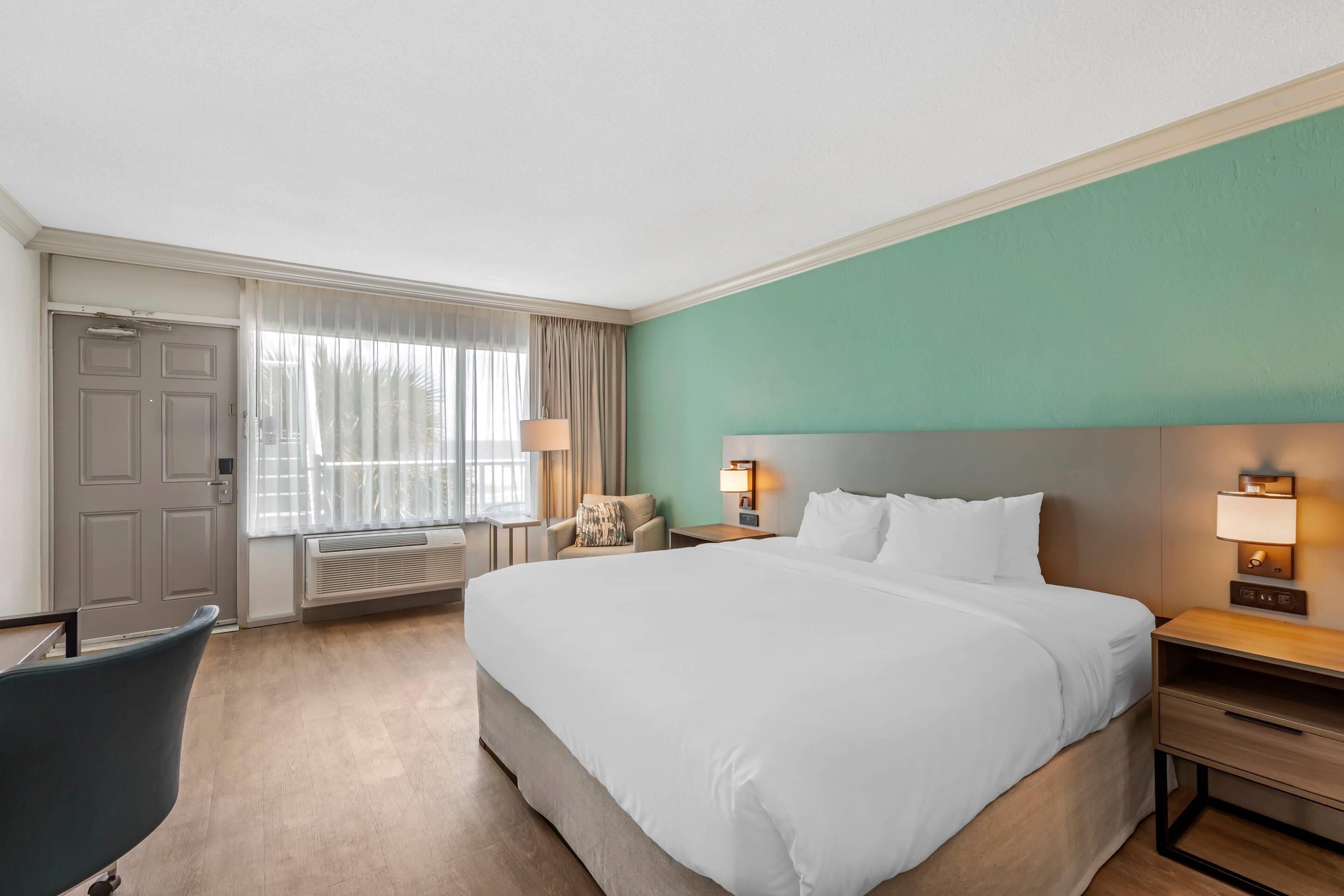 Une chambre d’hôtel avec un grand lit, une chaise, un bureau et une fenêtre avec des rideaux.