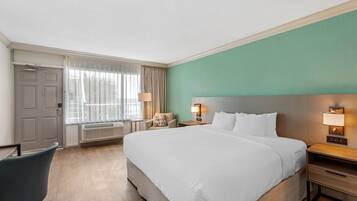 Une chambre d’hôtel avec un grand lit, une chaise, un bureau et une fenêtre avec des rideaux.