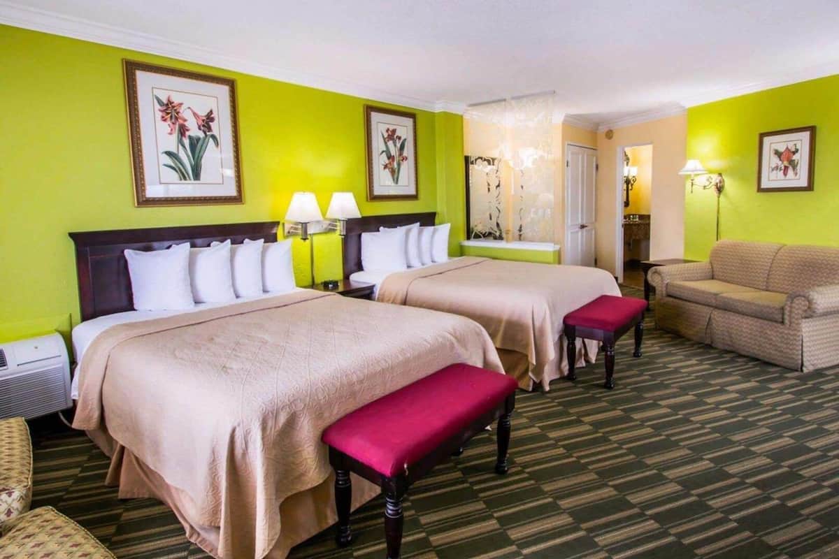 Quarto de hotel com duas camas, um banco, um sofá e obras de arte nas paredes.