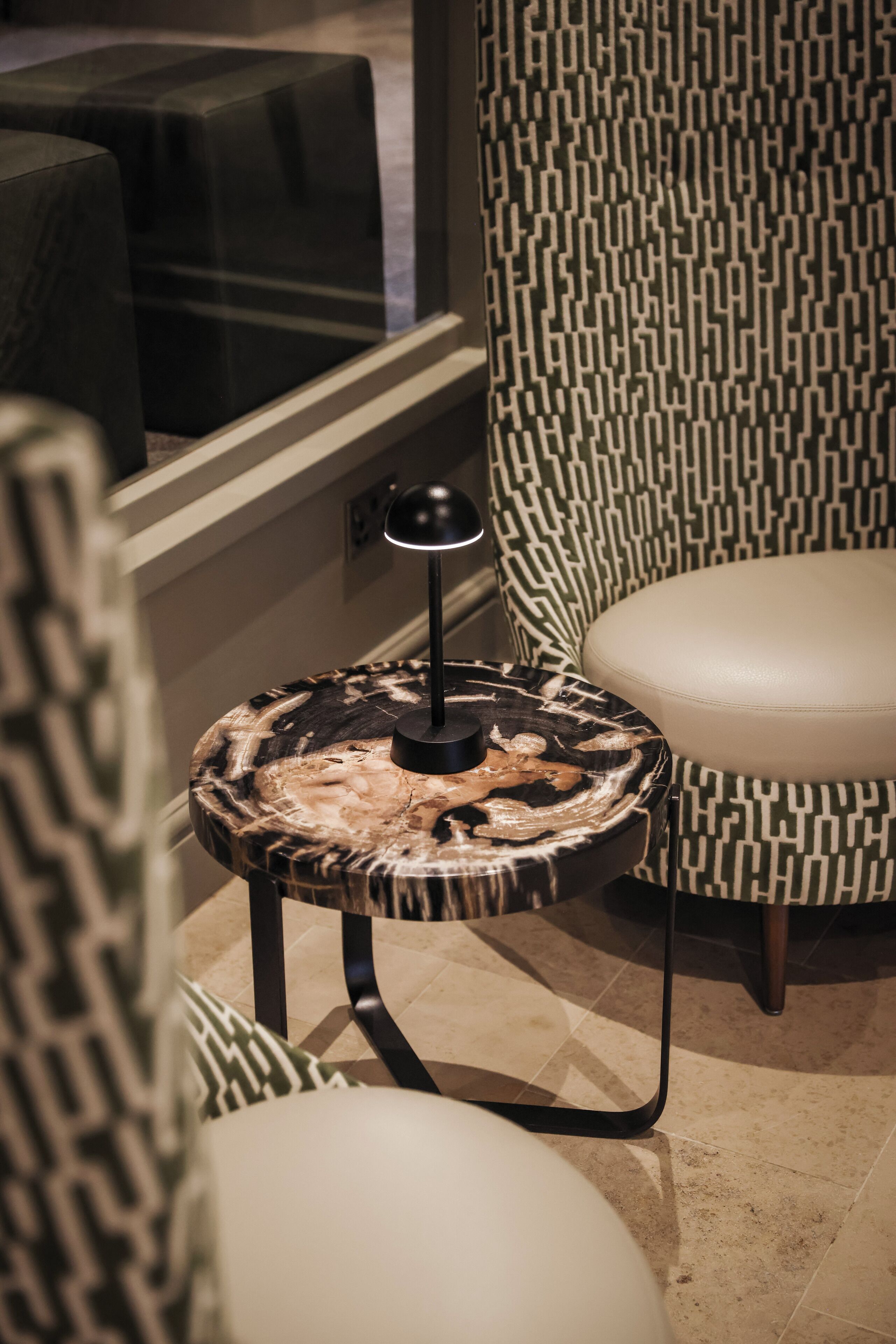 A modern interior with a patterned chair, a round table with a unique wood design, and a small lamp.
