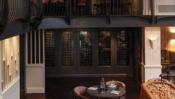A dining area with a long table, chairs, and a sofa. There is a balcony with a railing and a view of the interior.