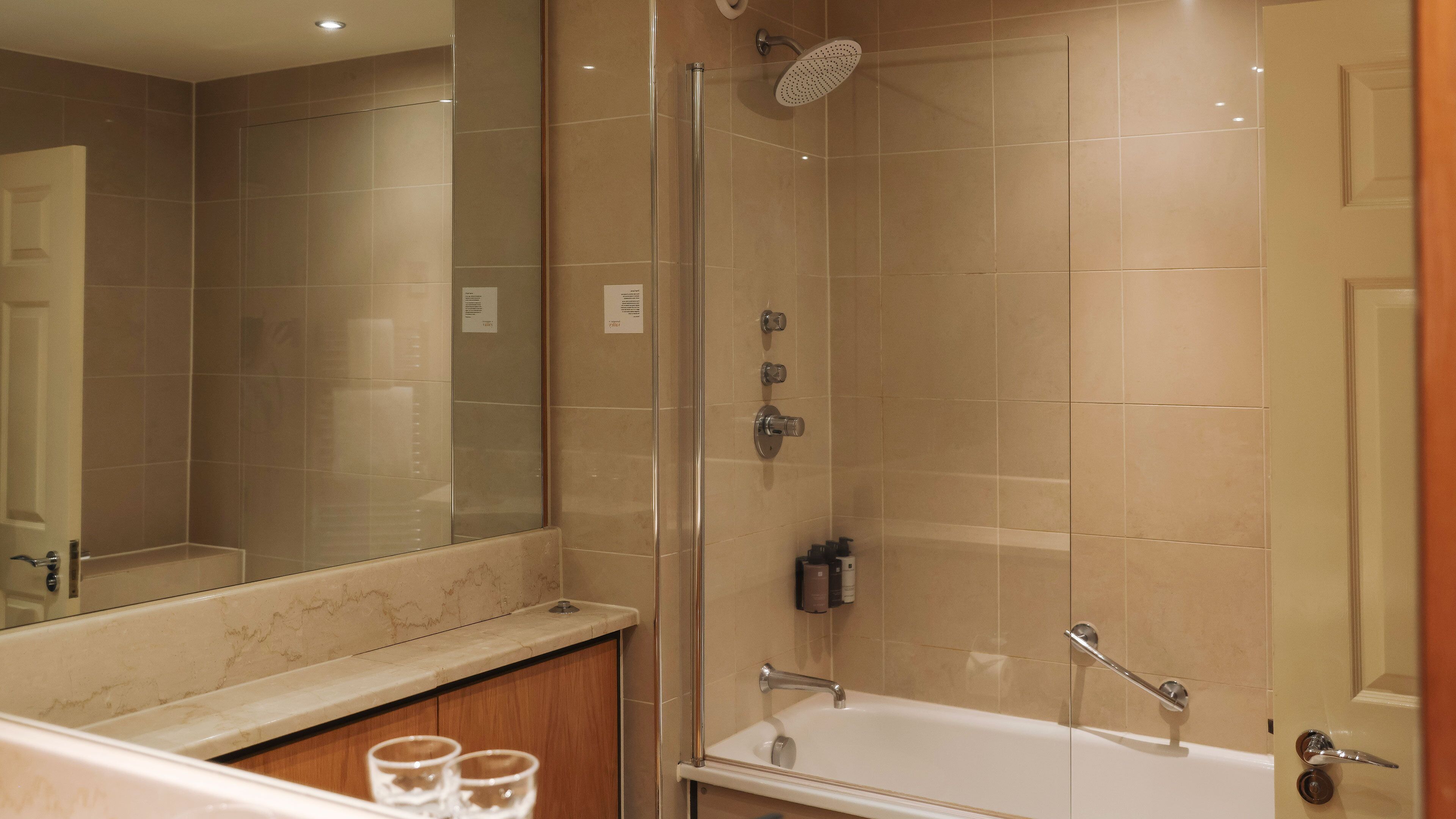 A modern bathroom with a glass shower enclosure, a large mirror, and a bathtub.