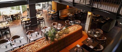 Un restaurante amplio con varias zonas de comedor, incluyendo una zona central con una mesa larga y una zona más pequeña con mesas redondas.